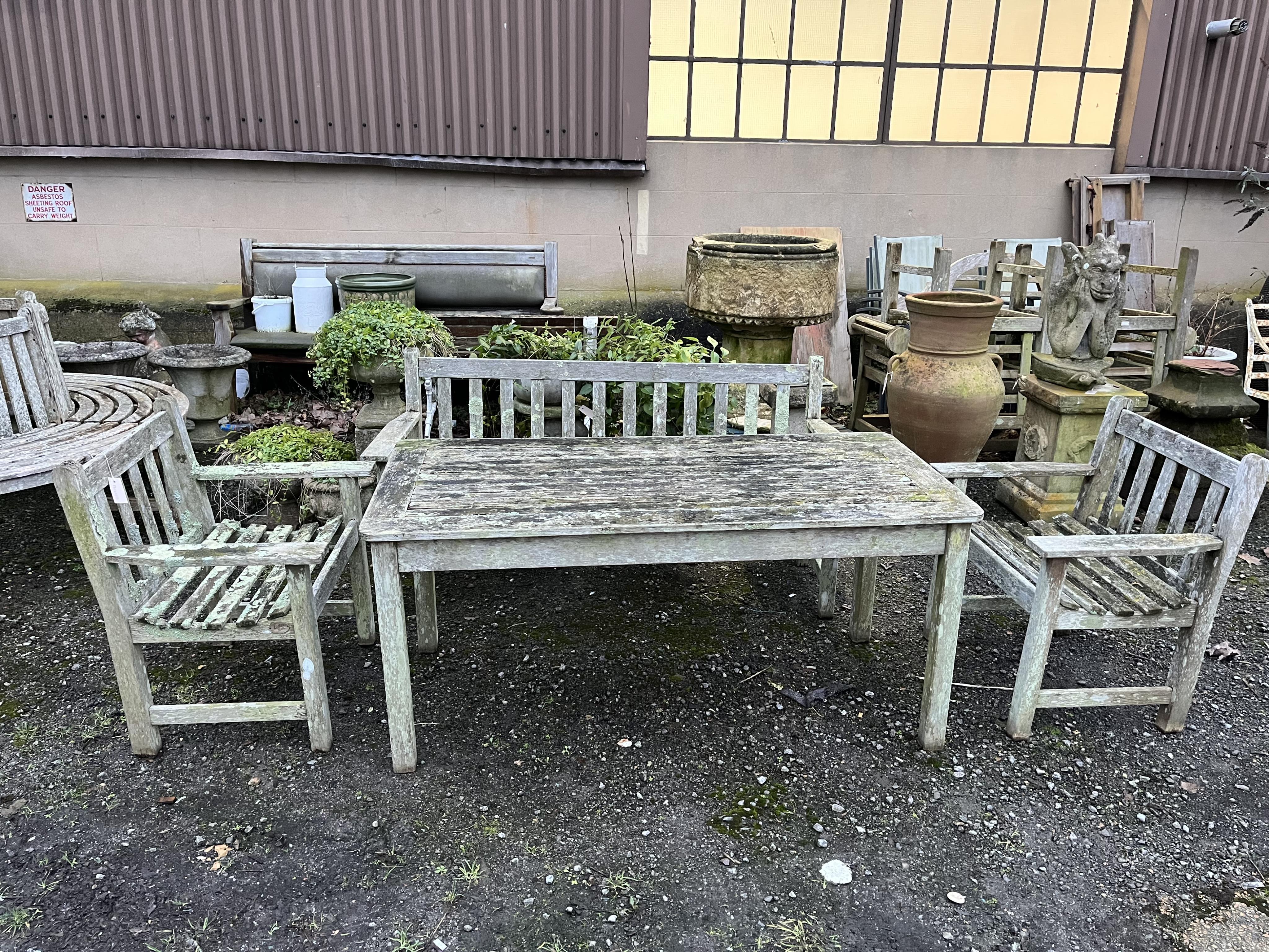 A slatted weathered teak rectangular garden table, width 149cm, depth 70cm, height 68cm, a bench and two armchairs. Condition - fair